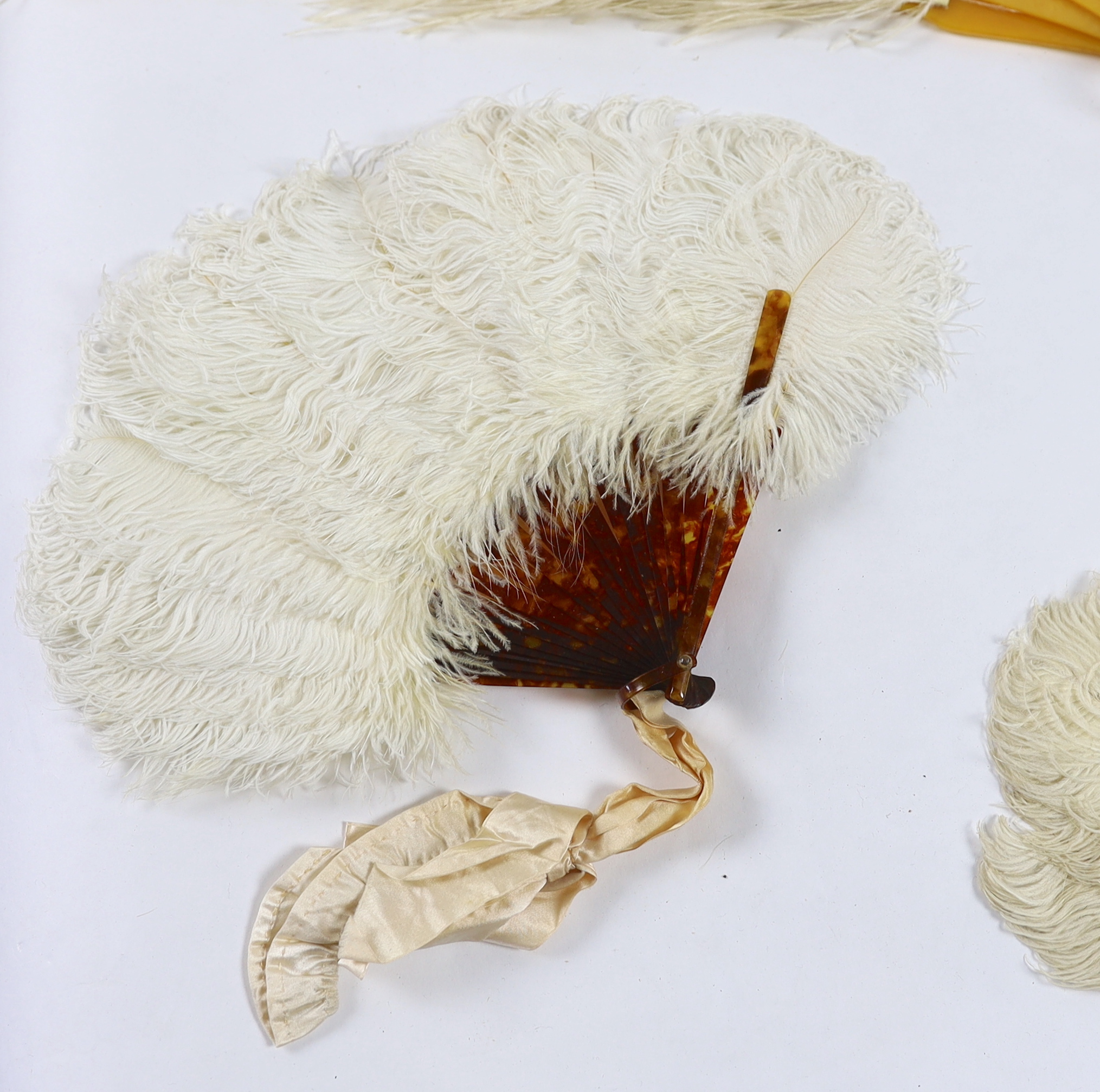 Two early 20th century Ostrich feather and mother of pearl fans, another similar fan with amber Bakelite handle and a small tortoiseshell and feather fan (4)